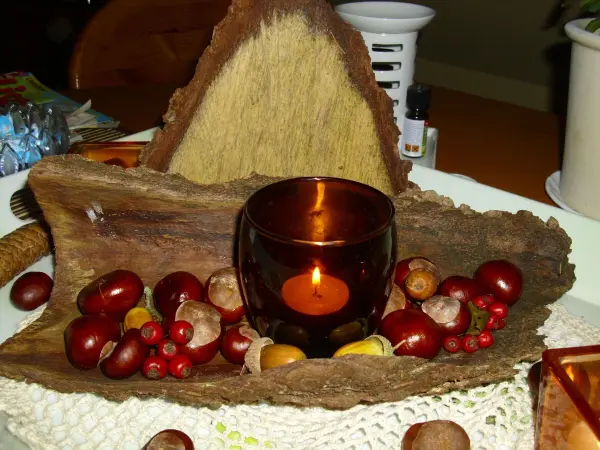Ein rustikales Holzstück dient als Basis für eine Herbst-Tischdeko, umgeben von Eicheln und Kastanien, mit einer Kerze in der Mitte.