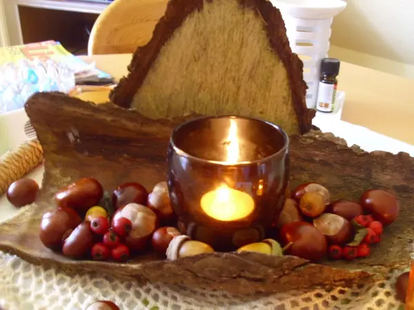 Eine rustikale Tischdeko aus Naturmaterialien zeigt eine Kerze in einem Holzgefäß, umgeben von Nüssen und einem warmen Ambiente.