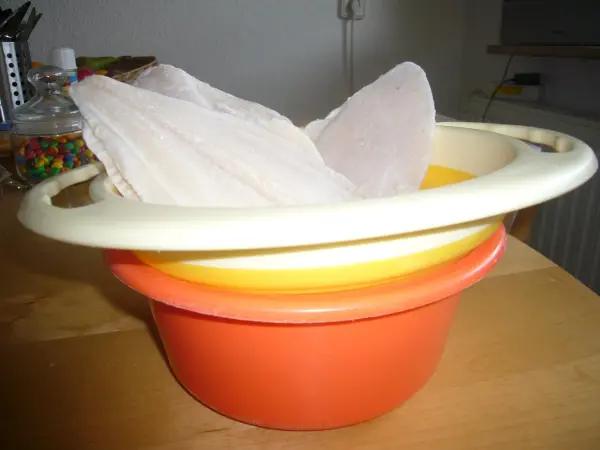 Ein orangefarbener Behälter hält gefrorenes Geflügel, während es im Wasser gefriert, auf einem Tisch in einer Küchenumgebung.