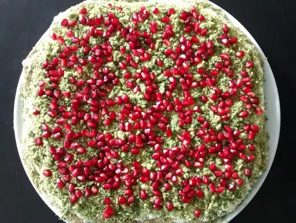 Ein Mooskuchen mit Blattspinat, dekoriert mit leuchtend roten Granatapfelkernen, steht auf einem weißen Teller.