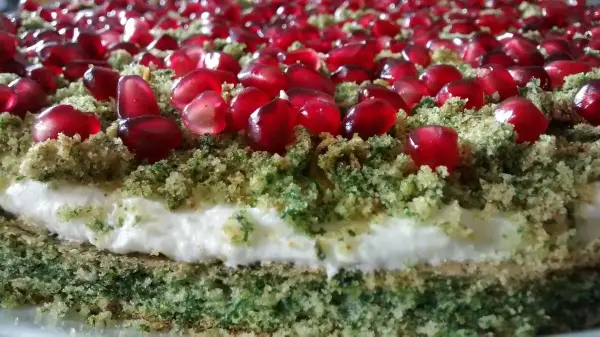 Ein Mooskuchen mit Blattspinat, dekoriert mit roten Granatapfelkernen, liegt auf einem weißen Teller.