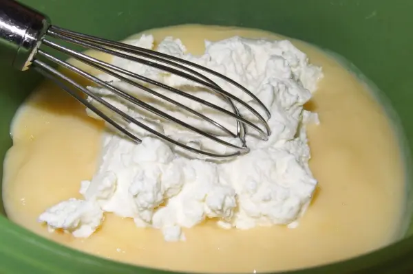 Eine Schüssel mit Käsekuchen-Mischung, in der ein Schneebesen die Zutaten verbindet, um einen leckeren Nachtisch zuzubereiten.