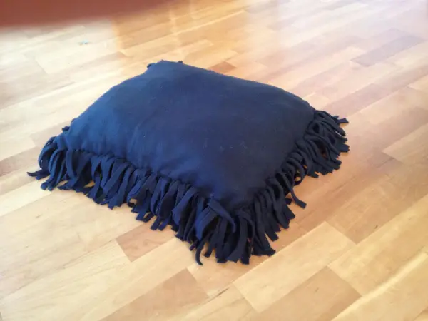 Ein Kissen für Hund und Katze liegt auf einem Holzboden, mit fransigen Kanten, bereit für den Gebrauch.