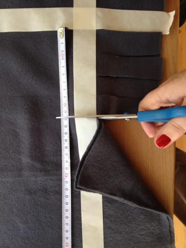 Ein Handwerker schneidet mit einer Schere ein graues Stück Stoff für Kissen für Hund und Katze auf einem Tisch.