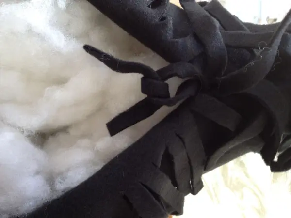 Ein schwarzes Kissen mit fransigen Kanten wird mit einer weichen Füllung gefüllt, auf einer hellen Oberfläche liegend.