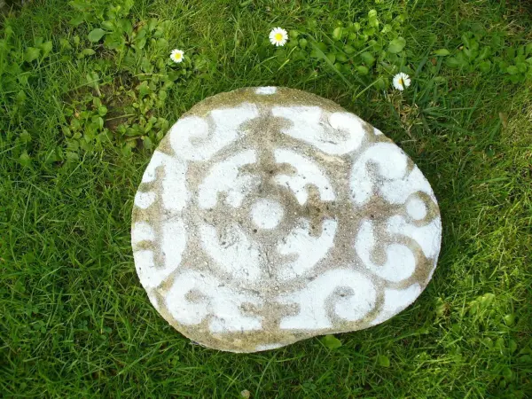 Eine verzierte Beton Gehwegplatte liegt auf grünem Gras, geschmückt mit einem eleganten Muster in Weiß.