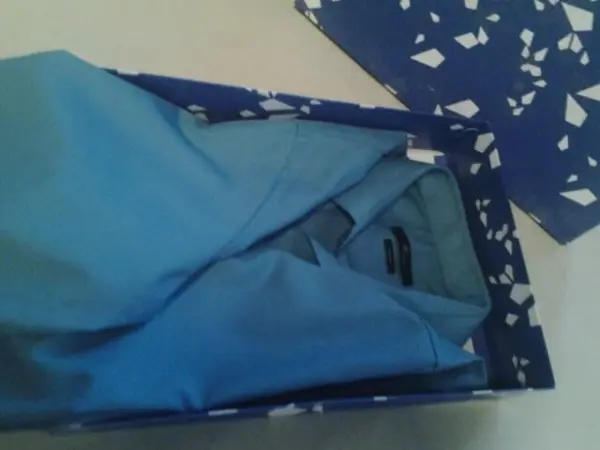 Ein blaues Hemd liegt ordentlich gefaltet in einer Geschenkbox, umgeben von gemustertem Geschenkpapier.