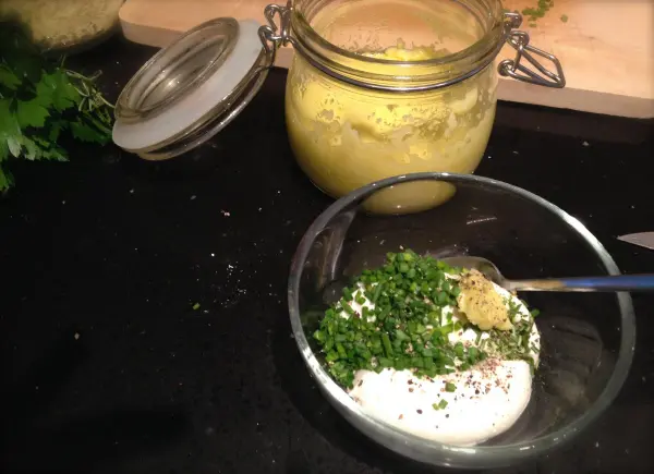 Ein Schüsselchen mit einer Kräutercreme aus Joghurt und frischen Kräutern wird zubereitet, daneben ein Glas mit püriertem Kürbis.