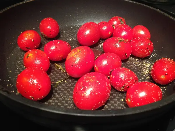 Rote Kirschtomaten liegen in einer schwarzen Pfanne und werden sanft erhitzt, um intensiven Geschmack zu entwickeln.