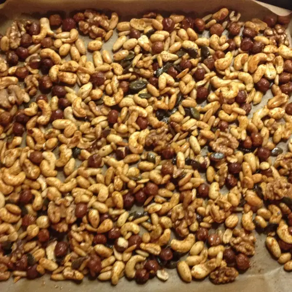 Geröstete Gewürznüsse mit Chili und Honig liegen gleichmäßig auf einem Backblech in einer warmen Küche.