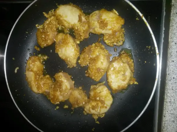 Hühnerfleischstücke braten in einer Pfanne, auf einem Herd in einer Küche. Sie sind goldbraun und paniert.