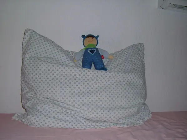 Ein Federbett mit einem bunten Kissenbezug liegt auf einem Bett, während ein Spielzeug darauf sitzt.