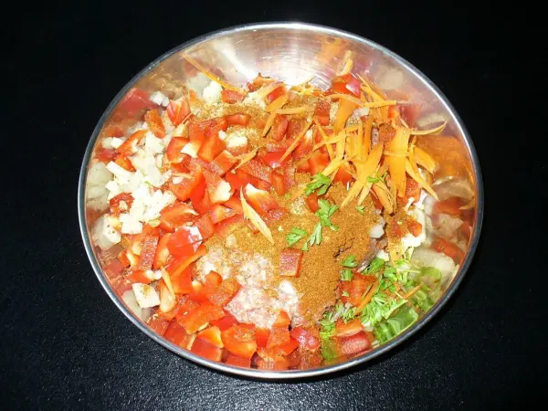 Eine Schüssel mit geschnittenem Gemüse, darunter Paprika, Karotten und Zwiebeln, ist bereit für die Zubereitung von Frikadellen.