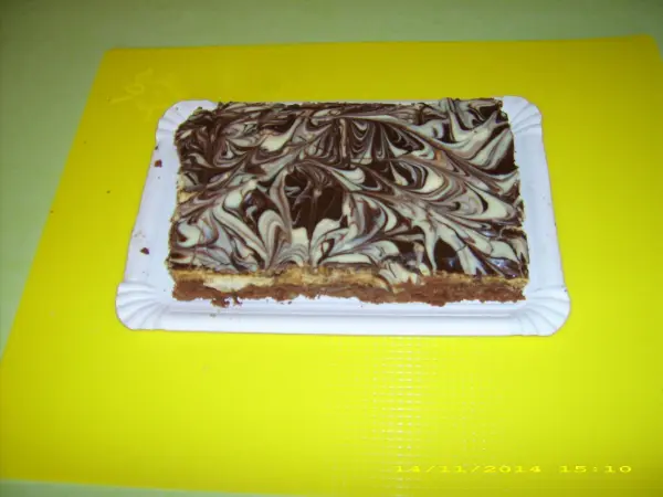 Ein Schoko-Karamell-Kuchen liegt auf einem weißen Teller, kunstvoll marmoriert, vor einem gelben Hintergrund.