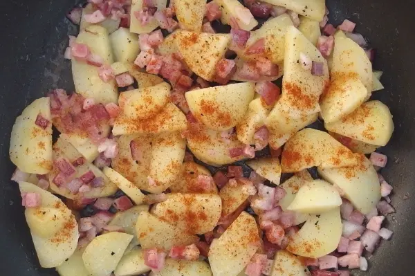 Goldbraune Bratkartoffeln werden in einer Pfanne mit gewürfeltem Schinken und Paprikagewürz zubereitet.
