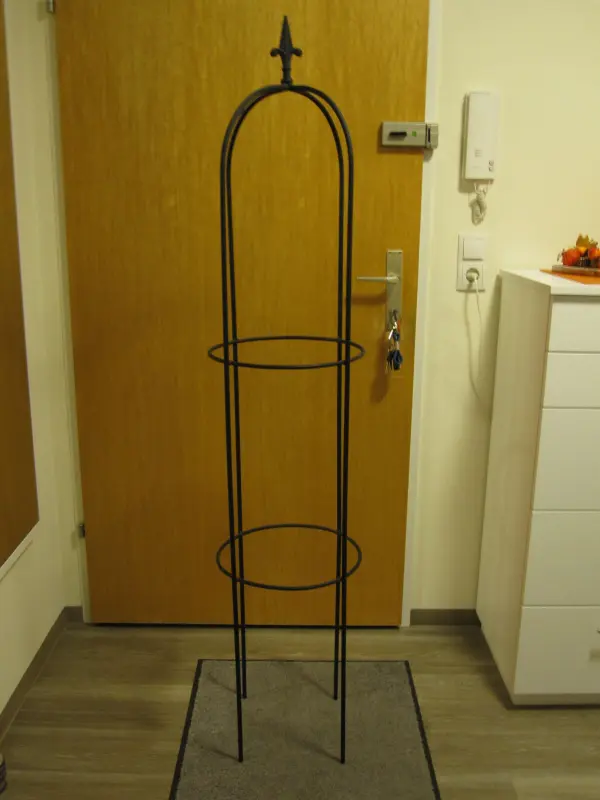 Eine schmiedeiserne Struktur steht auf einem Teppich neben einer Tür und dient als alternative Weihnachtsbaum-Dekoration.