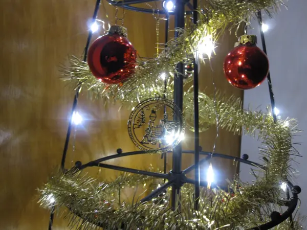 Ein dekorativer Weihnachtsbaum aus einem Metallgerüst ist mit Weihnachtslichtern, goldenem Lametta und roten Kugeln geschmückt.