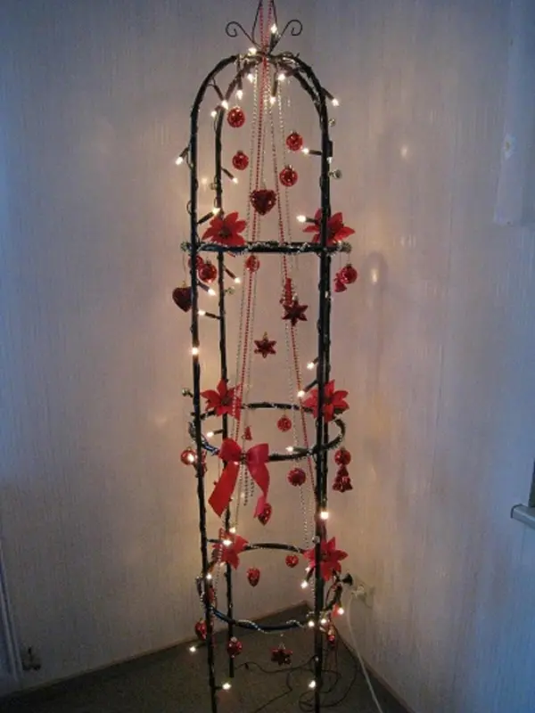 Ein dekorativer Weihnachtsbaumersatz steht hell erleuchtet in einem Raum, geschmückt mit roten Ornamenten und Lichtern.