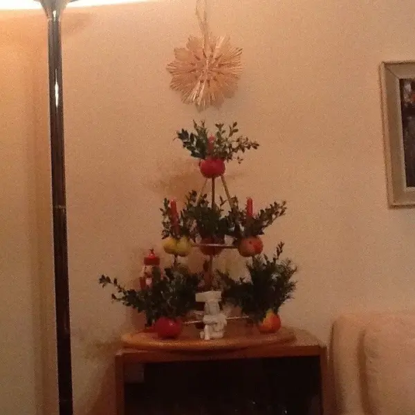 Ein dekorativer Weihnachtsbaum aus Früchten und Zweigen steht auf einem Tisch in einem gemütlichen Raum mit sanfter Beleuchtung.
