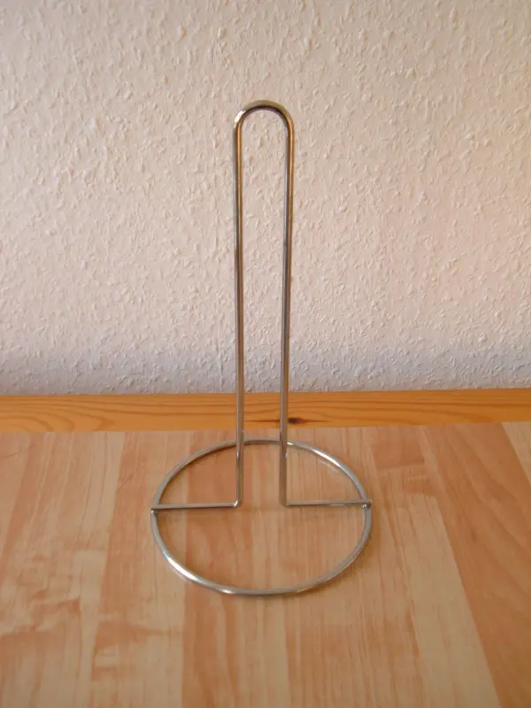 Ein Gitarrenhalter aus Metall steht auf einem Holzregal, bereit zur Wandmontage für die sichere Aufbewahrung einer Gitarre.