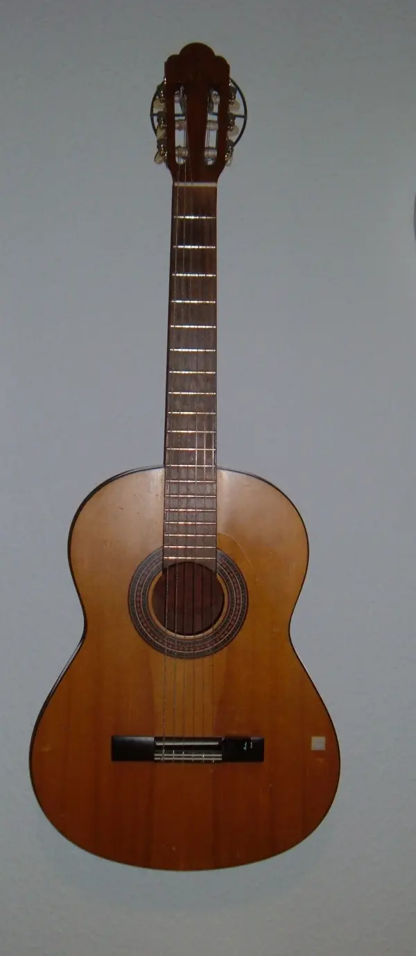 Eine Wandhalterung für eine Akustikgitarre ist an einer hellen Wand montiert, während die Gitarre elegant präsentiert wird.