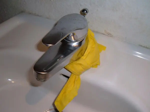 Ein Wasserhahn mit Kalkrändern wird mit einem gelben Tuch gereinigt, um die Armatur zu säubern.