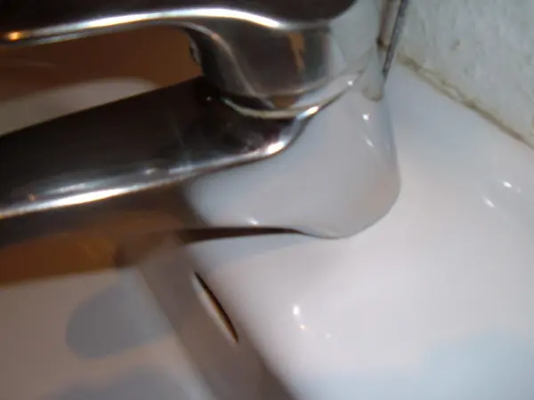Ein glänzender Wasserhahn sitzt über einer weißen Waschbecken-Oberfläche, ohne Kalkränder sichtbar.