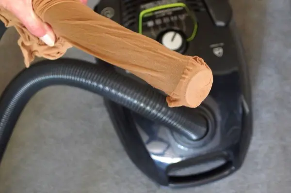 Ein Staubsauger wird benutzt, um kleine Teile wie Ohrringe aufzunehmen, während ein Socken über das Schlauchende gezogen wird.