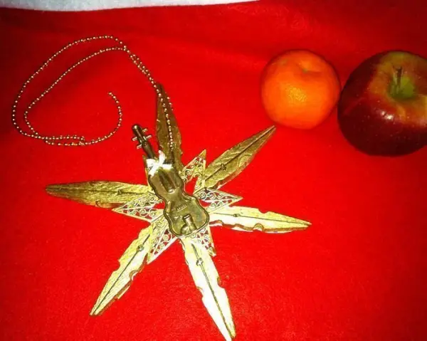 Ein Stern aus Wäscheklammern liegt auf einem roten Tisch, umgeben von einer Orange und einem Apfel, funkelt festlich.