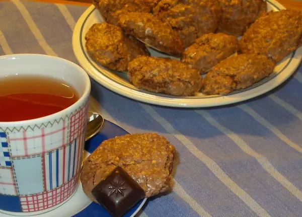 Ein Teller mit Schokoladenmakronen steht auf einem Tisch, neben einer Tasse Tee, auf einem gestreiften Tischdecken.