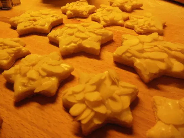Sternförmige Butter-Mandel-Sterne liegen auf einem Holzbrett, dekoriert mit Mandelsplittern, in gemütlicher Küchenszene.