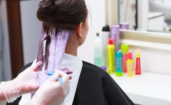 Eine Person mit gefärbten Haaren erhält eine Behandlung zur Entfärbung, um die Haarfarbe zu verändern, umgeben von Pflegeprodukten.
