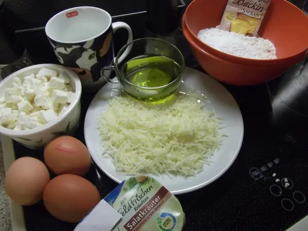 Eine Vielzahl von Zutaten für einen Feta-Kuchen mit Kräutern liegt auf einer Arbeitsfläche, bereit zum Zubereiten.