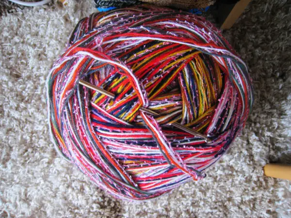 Ein runder Knäuel aus buntem Garn liegt auf einem Teppich, bereit zum Stricken dicker Socken als Hausschuhe.