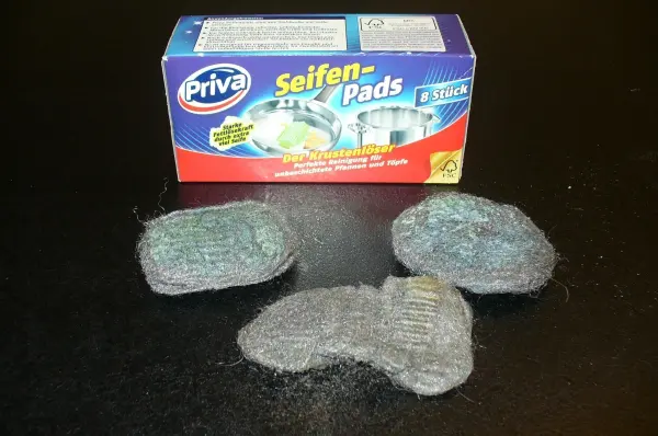 Drei Stahlwolle-Pads liegen vor einer Verpackung, die zur effektiven Entfernung von Rost am Fahrrad verwendet werden kann.