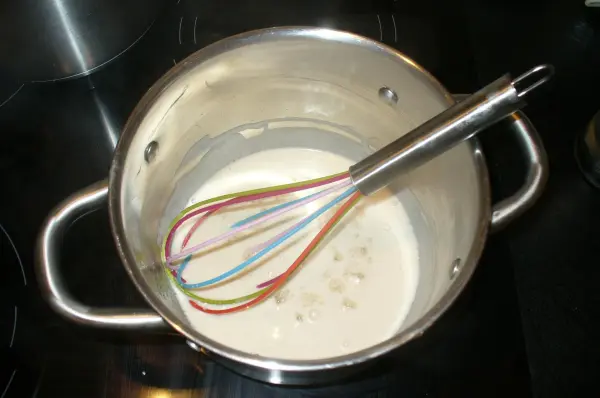 In einem Topf wird ein cremiger Kuchenmix mit einem bunten Schneebesen verrührt, um leckere Kuchen im Glas zuzubereiten.