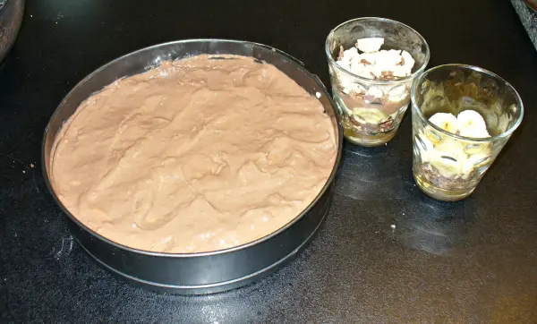 Ein runder Kuchen und zwei Gläser mit Schichten aus Kuchen, die in einer modernen Küchenumgebung präsentiert werden.