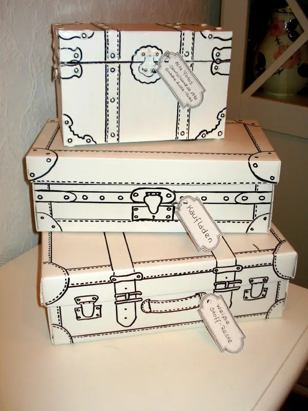Drei shabby chic Kartons im Kofferlook stapeln sich dekorativ auf einer weißen Oberfläche, umgeben von einem hellen Raum.