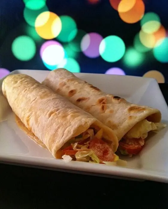 Zwei Wraps mit Thunfischfüllung liegen auf einem weißen Teller, umgeben von verschwommenen, bunten Lichtern.
