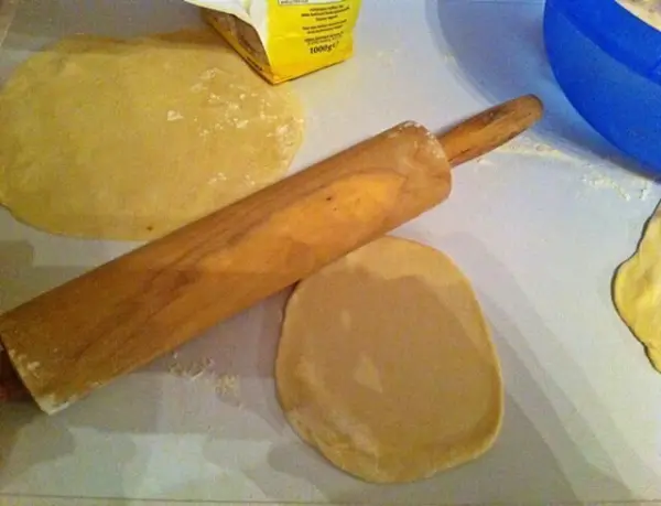 Eine Holzrolle rollt dünn ausgerollte Teigstücke auf einer Arbeitsfläche, um Wraps mit Thunfischfüllung zuzubereiten.