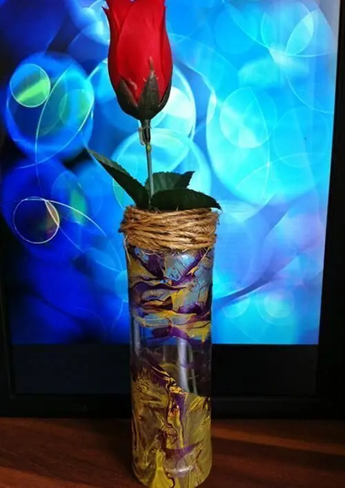 Eine dekorative, unifarbene Vase mit Nagellackmustern hält eine rote Rose und steht vor einem farbigen, verschwommenen Hintergrund.