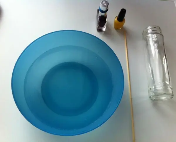 Ein großer blauer Behälter steht auf einem Tisch, neben Nagellackfläschchen und einem Holzstab zum Verzieren.