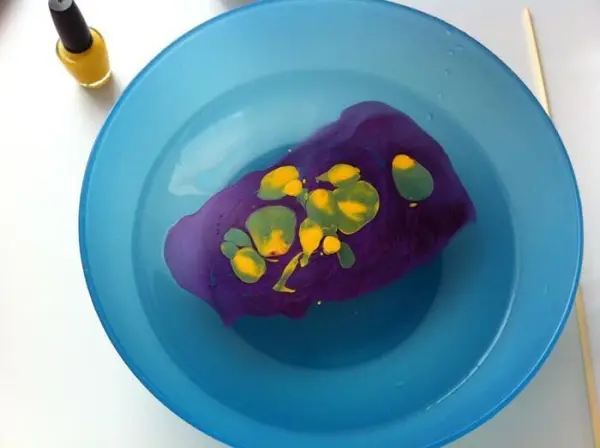Eine blaue Schüssel enthält bunten Nagellack, der kreativ auf eine unifarbene Vase aufgetragen wird.