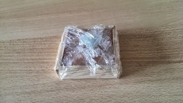 Ein Labyrinth-Spiel mit einer Kugel auf einer Holzplatte, die in Frischhaltefolie eingewickelt ist, auf einem Tisch.