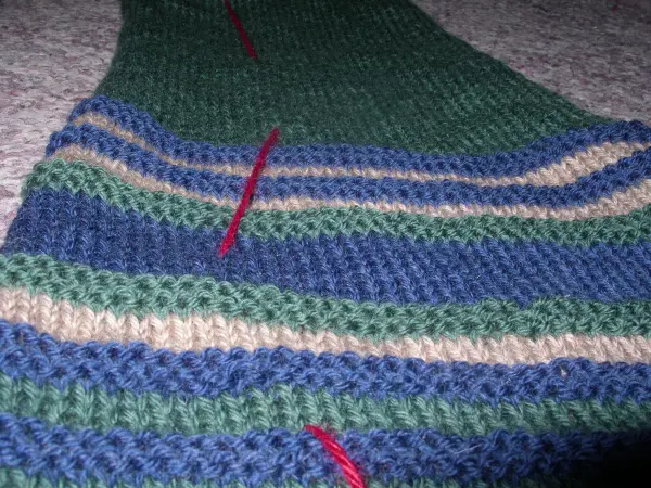 Ein gestreiftes Strickstück liegt flach auf einem grauen Untergrund, mit roten Markierungen für den psychologischen Trick.