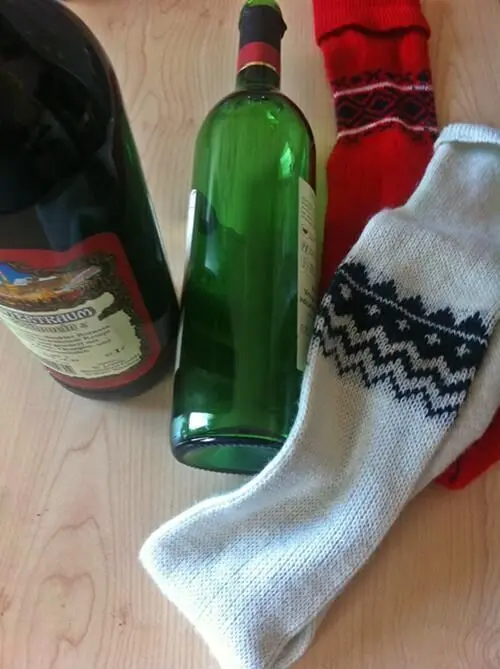 Eine grüne Flasche und eine braune Flasche sind winterlich in dekorativen Strümpfen auf einem Holzuntergrund platziert.