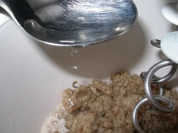 Eine Kelle schwenkt über eine Schüssel mit grobem Teig, während Karamellstückchen in die Mischung fallen.