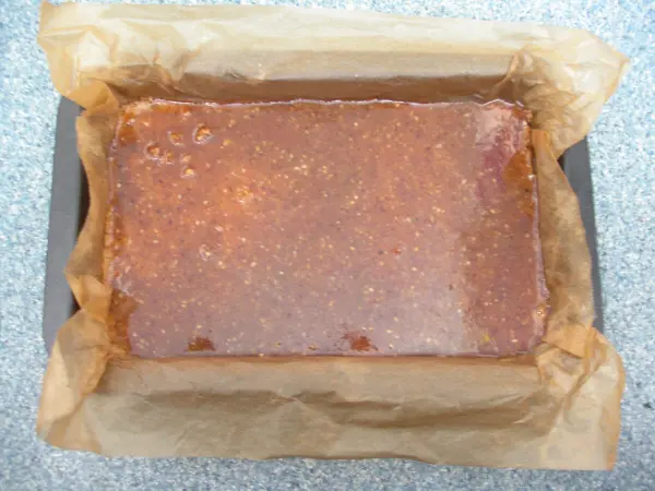 Ein glänzender Schoko-Karamell-Kuchen liegt auf Backpapier in einer Backform, bereit zum Servieren.