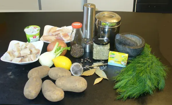 In einer Küche liegen Zutaten für einen schwedischen Fischtopf, darunter Kartoffeln, Fisch, Gewürze und frischer Dill.