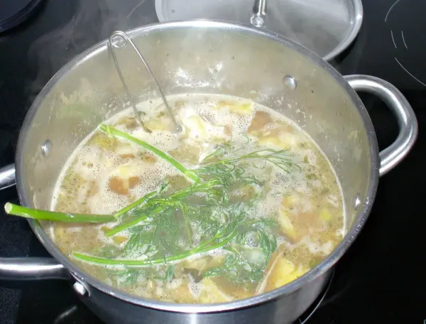 Ein silberner Topf über heißem Wasser kocht einen schwedischen Fischtopf mit frischen Kräutern, umgeben von einer modernen Küche.